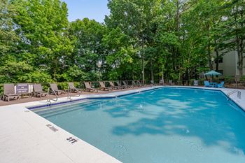 A swimming pool surrounded by trees and lounge chairs.